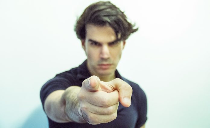 Man points at camera with an accusatory expression on his face. Federal employees ordered to report 'DEI' coworkers for termination